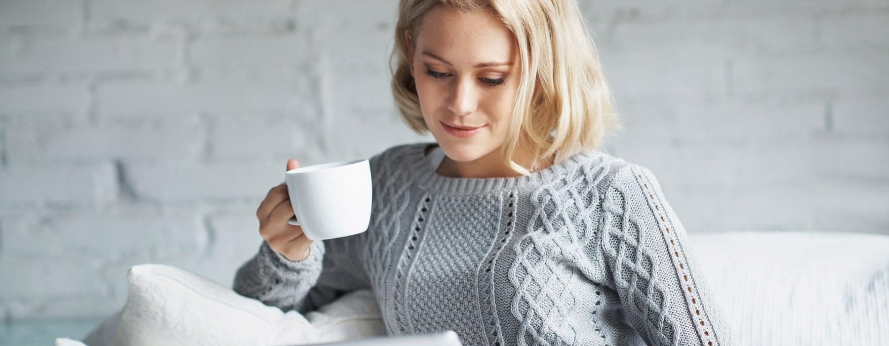 a woman holding a mug looking at a tablet