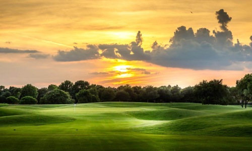a golf course with trees and a sunset