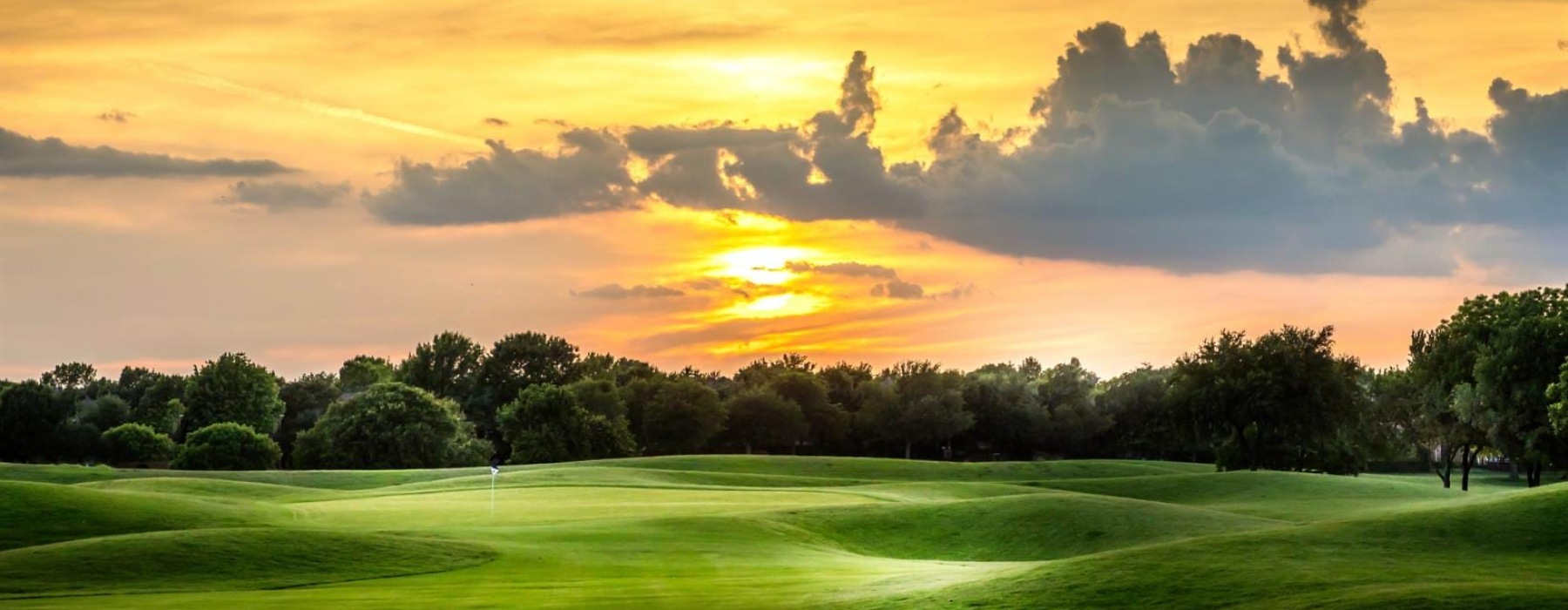 a golf course with trees and a sunset